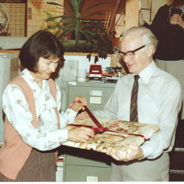A vintage picture of a happy looking older man and woman unwrapping a gift together.
