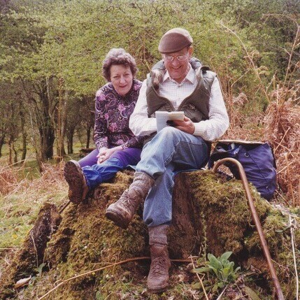 An older couple sitting together on a rocky mound in the country looking at a guidebook.