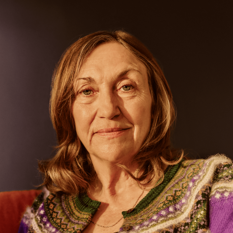 A close-up of a woman looking at the camera. She is sitting on a sofa at home.