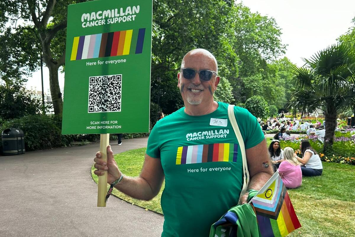 A man wearing sunglasses and green t-shirt in a park. He's holding a large sign that reads 