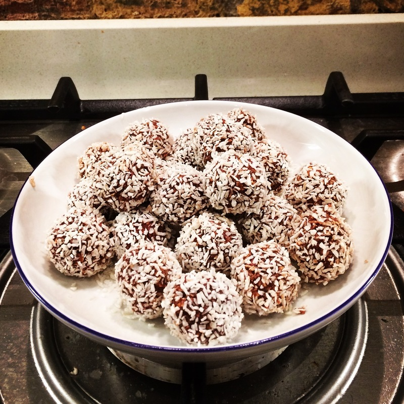A white bowl with a blue rim has with many Swedish chocolate balls in it. It is placed on a stove top.