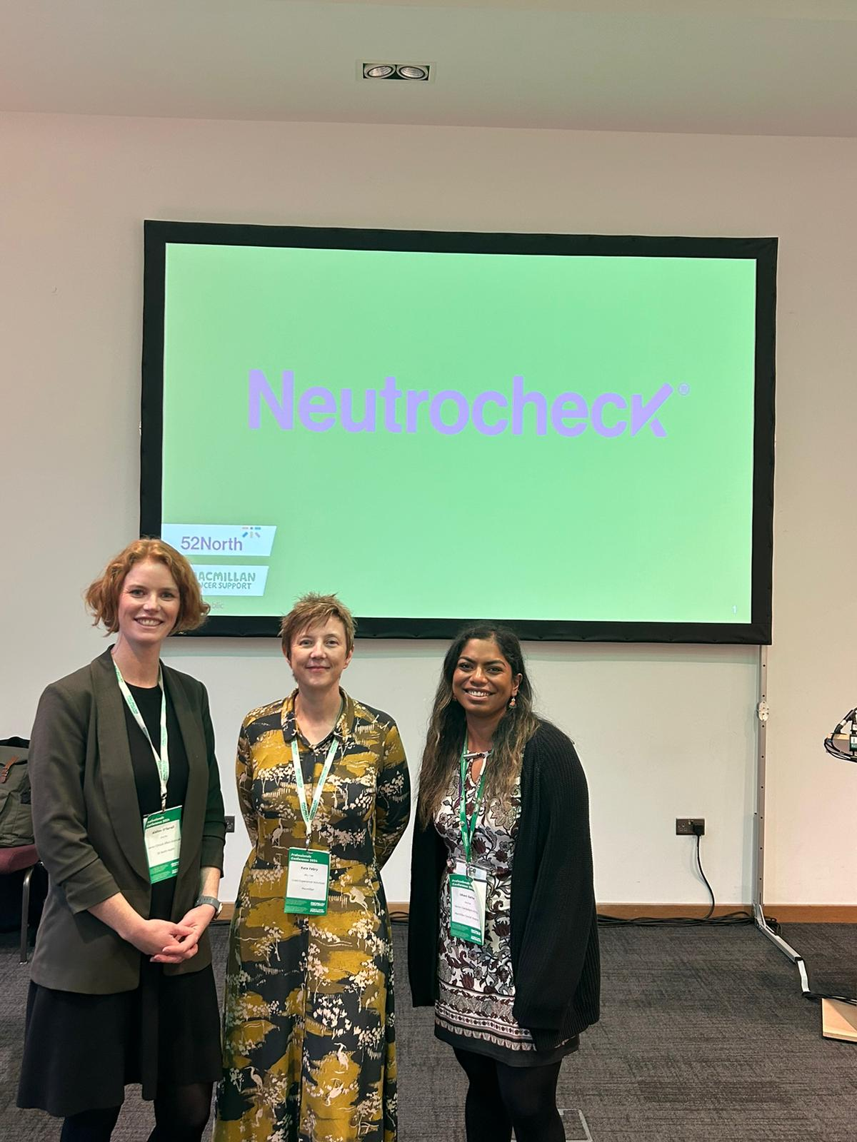 Three women standing in front of a screen with Neutrocheck written on it