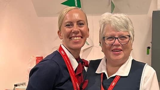 Two people are standing together arm in arm. They are wearing uniforms for work.