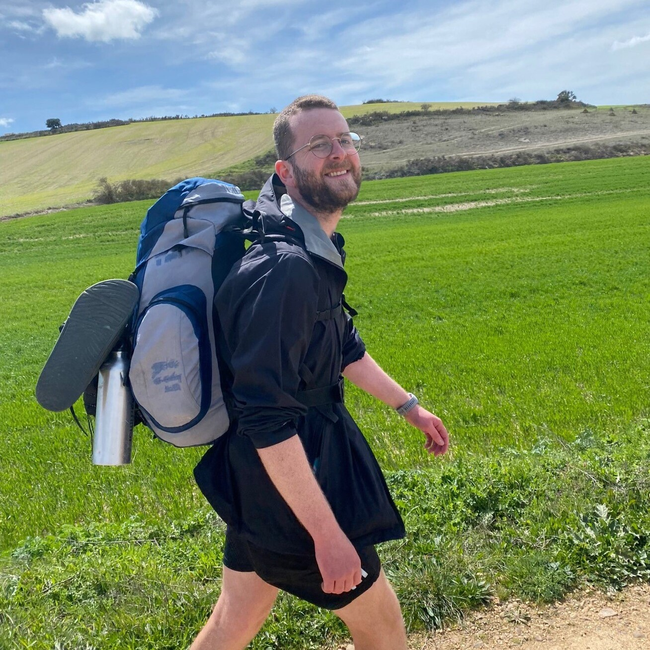 A man carrying a large backpack walks through the countryside.