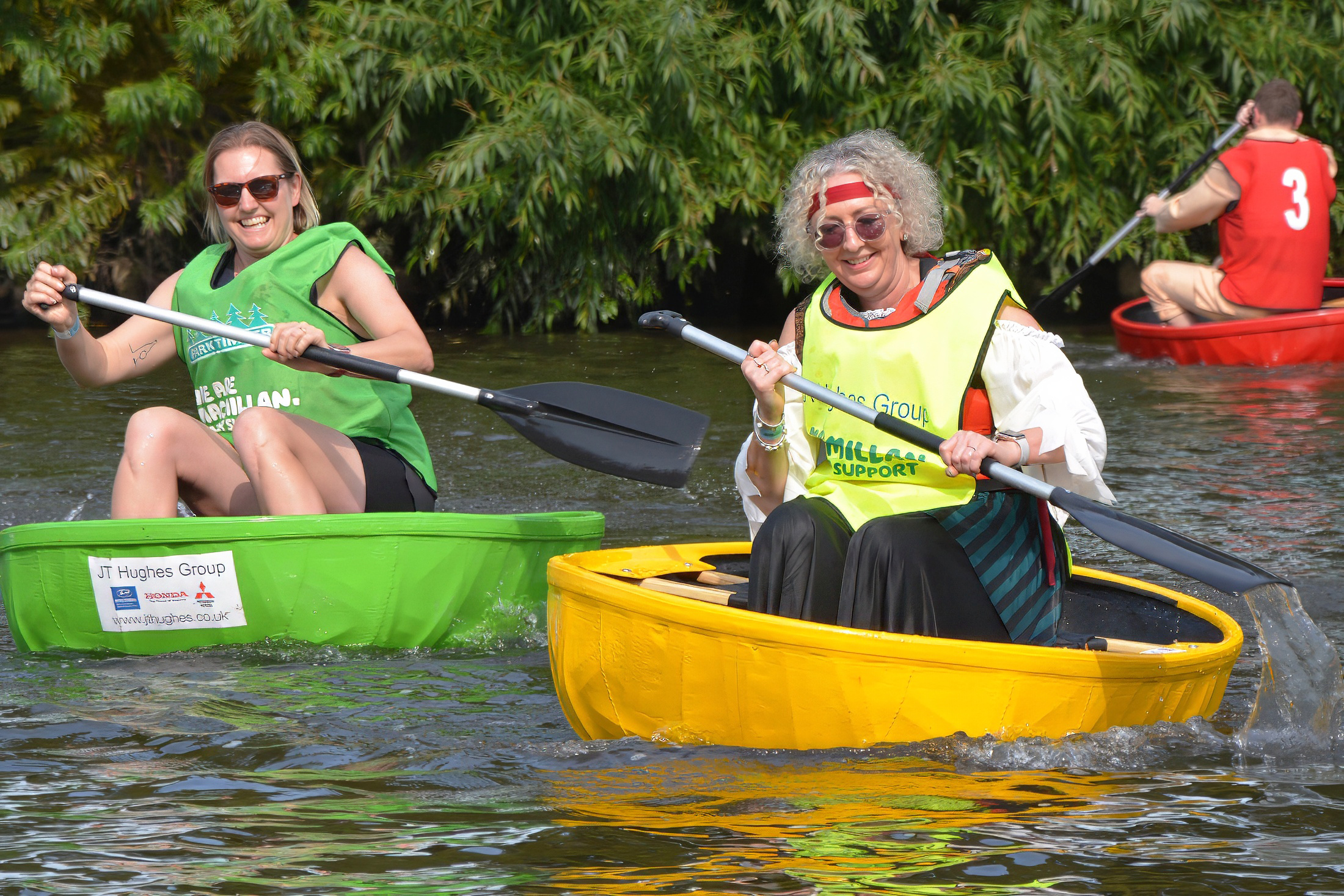 Two women wearing Macmillan bibs paddling their coracles