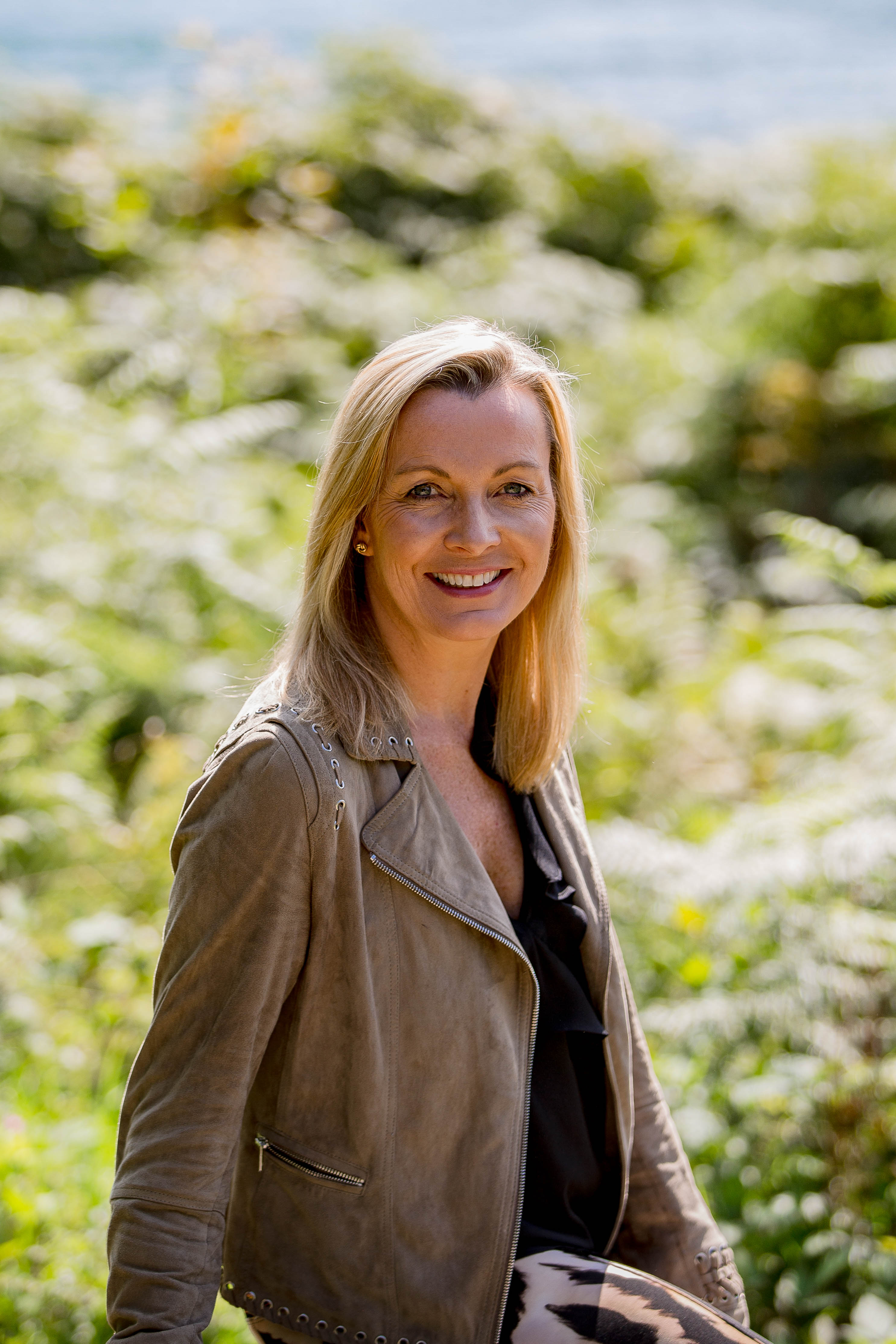Suki wearing a brown jacket looking at the camera and smiling