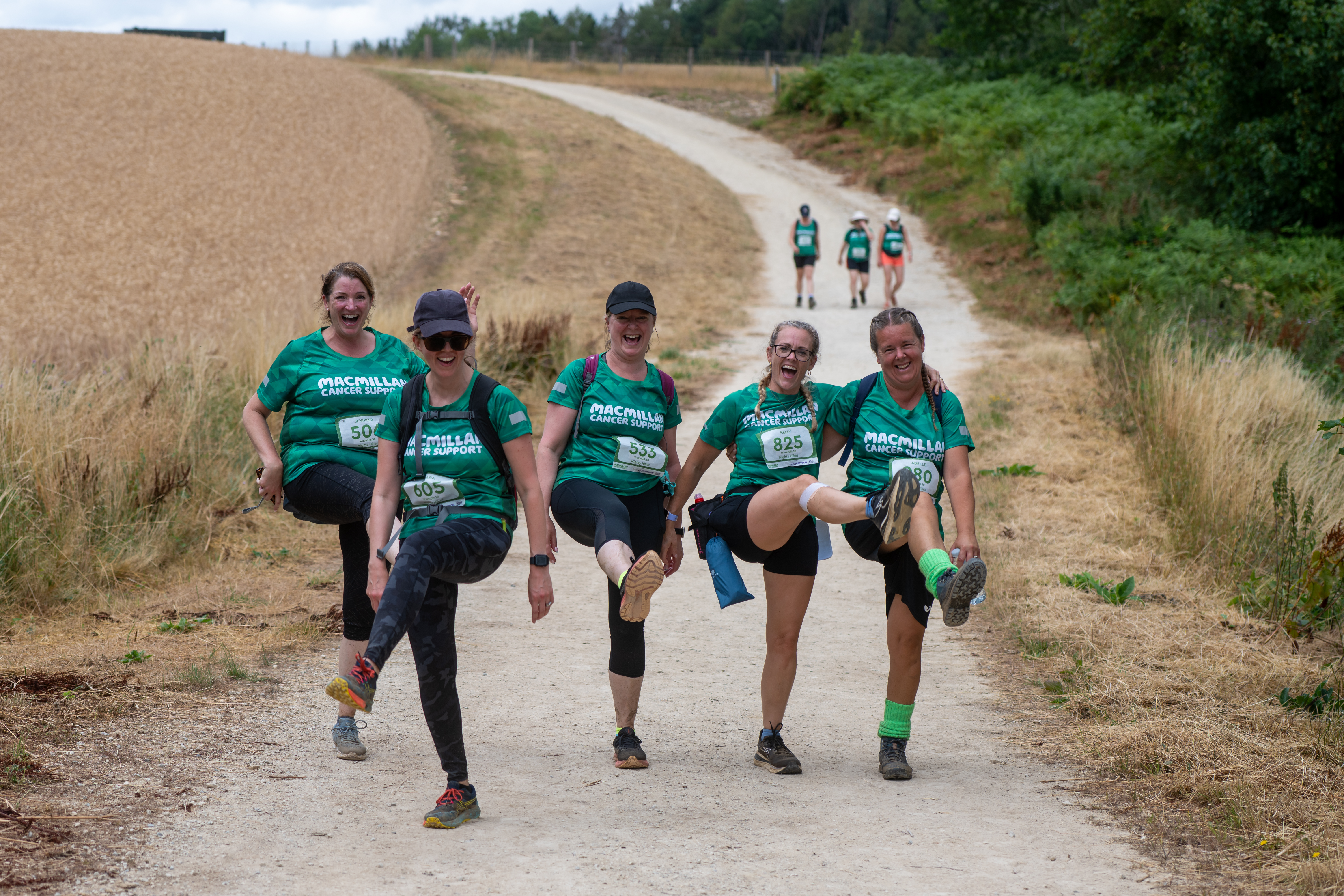 A team of five Mighty Hikers smiling at the camera and doing leg kicks