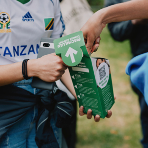People are placing coins in a Coffee Morning donation collection box. Photography by Rebecca Naen.