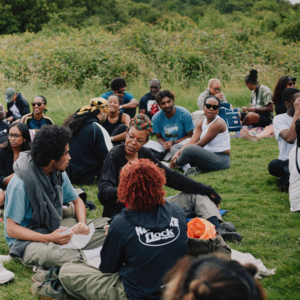 A group of people are sitting together in a field. They are talking in small groups.