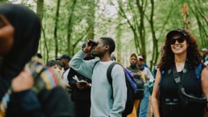 A group of bird watchers have gathered together in the woods. Some of them are using binoculars. Photography by Rebecca Naen.