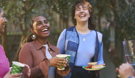 A group of people are standing together in a garden. They are laughing and enjoying themselves at a Coffee Morning. 