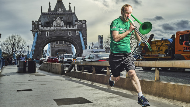 Nathaniel is captured mid leap in the air. He is playing a trombone and running across Tower Bridge. Photo by Julian Benjamin.