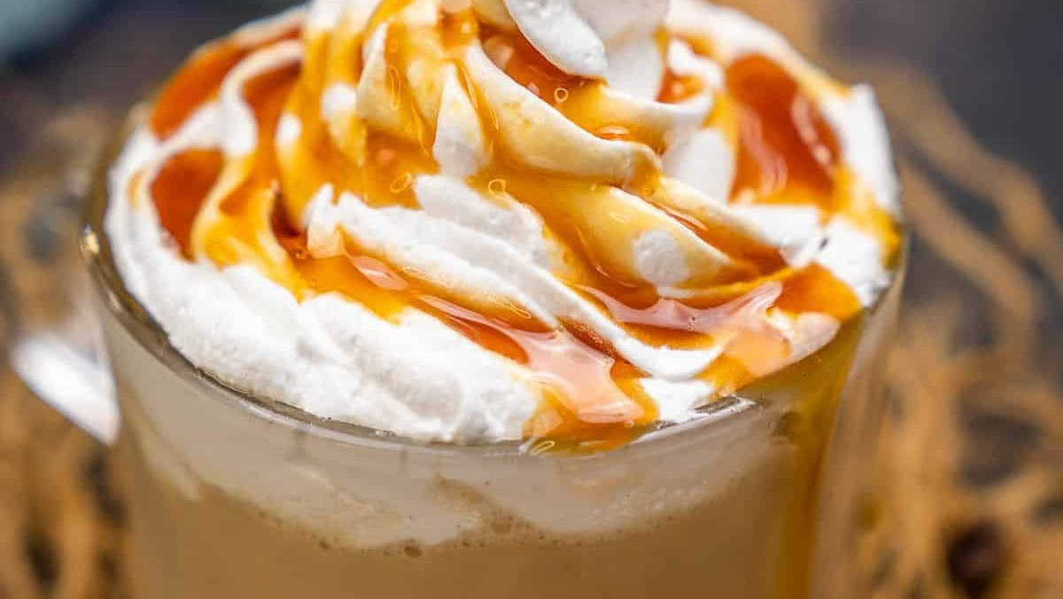 A large dollop of fresh whipped cream on top drizzled in caramel sauce placed in a glass coffee cup full of freshly brewed coffee.