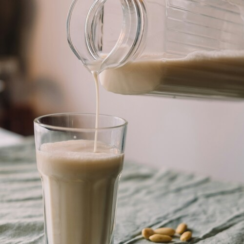 Someone is pouring a glass of milk alternative (nut based milk) from a glass jug into a glass cup. Photo by Kaja Sariwating on Unsplash.