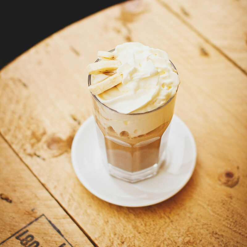 A glass cup is filled to the brim with coffee and a large dollop of fresh whipped cream. Photo by freestocks on Unsplash.