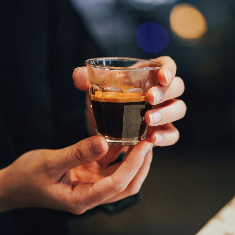 A person is holding qahwa in her hands. It is being served in a glass without handles. Photo by Jhunelle Francis Sardido on Unsplash.