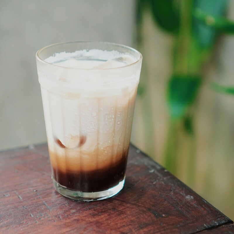 A fresh cup of kopi in a tall glass. It has condensed milk in it. Photo by Suryadhityas on Unsplash.