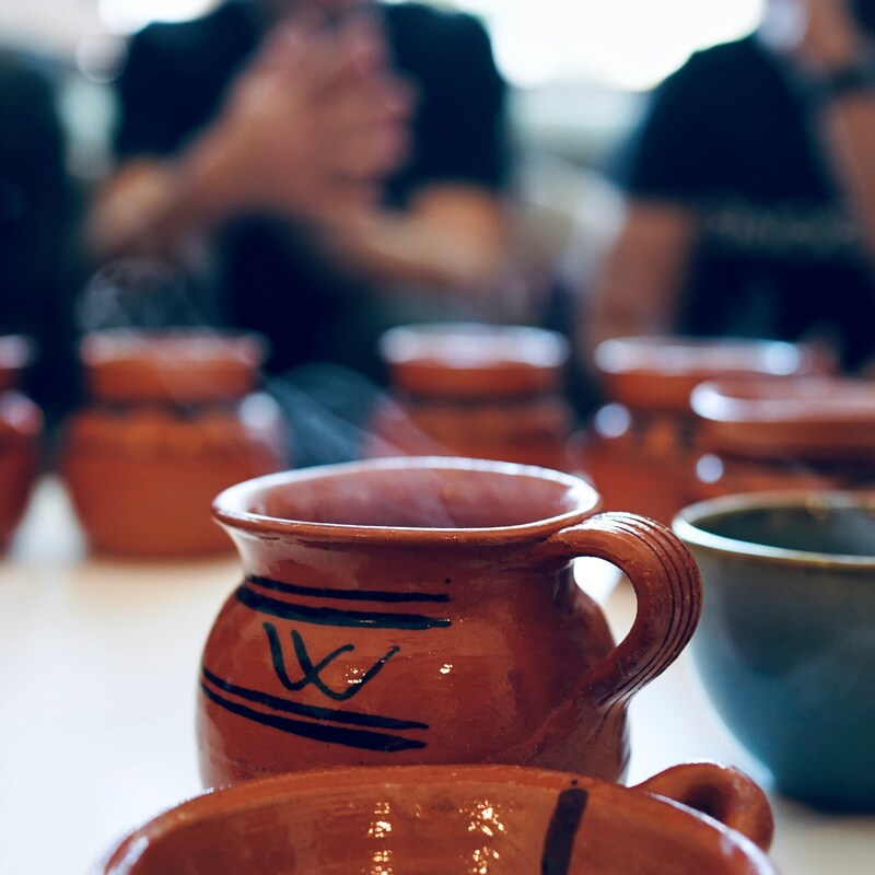 Coffee is being served in traditional Mexican ceramics on a table. The coffee is piping hot, with steam rising from it.