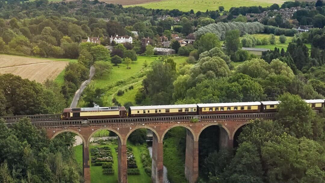 The Belmond British Pullman is travelling across a large bridge through the green countryside.