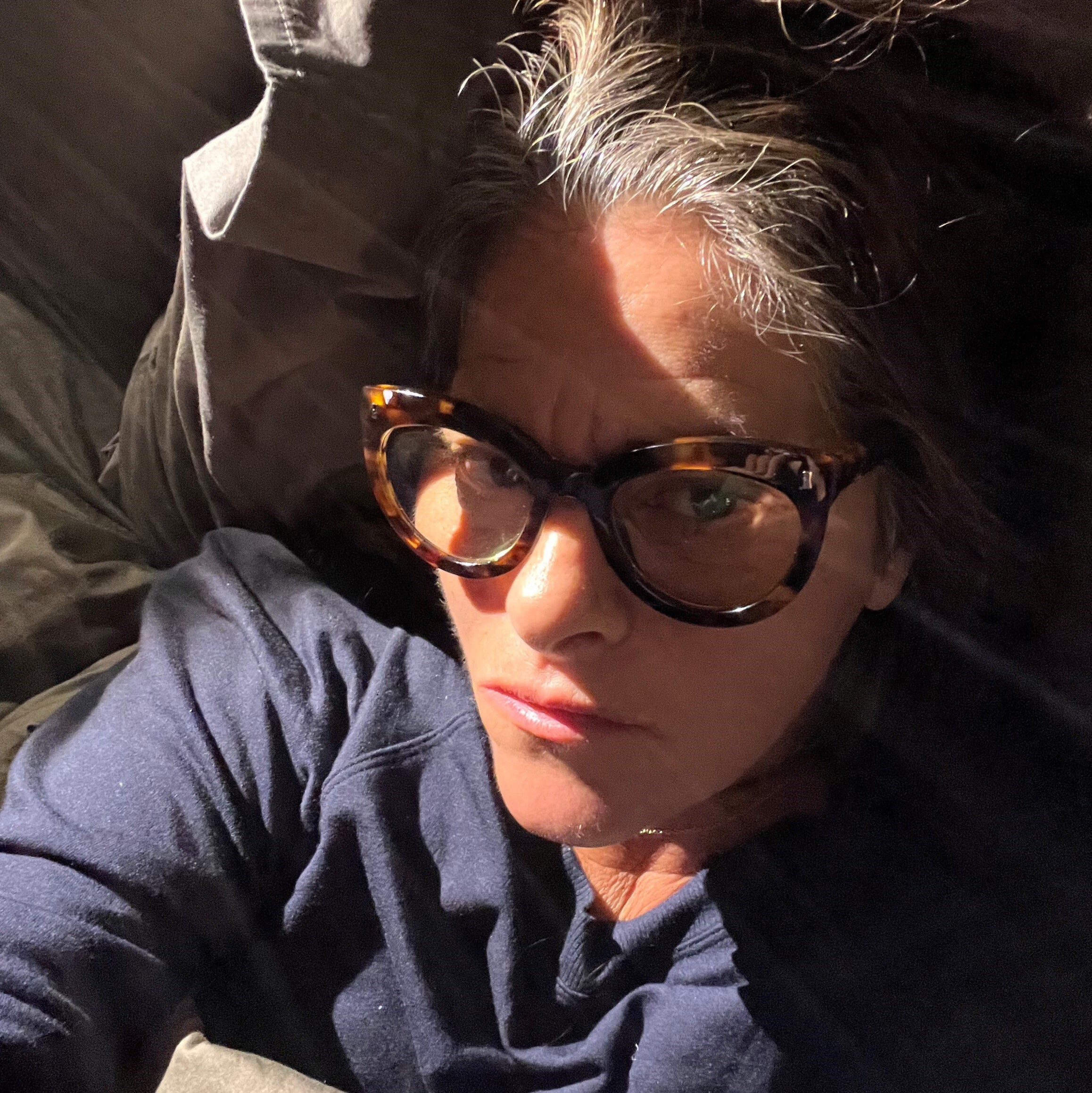 Artist Tracey Emin with glasses on and brown hair lying in bed., 