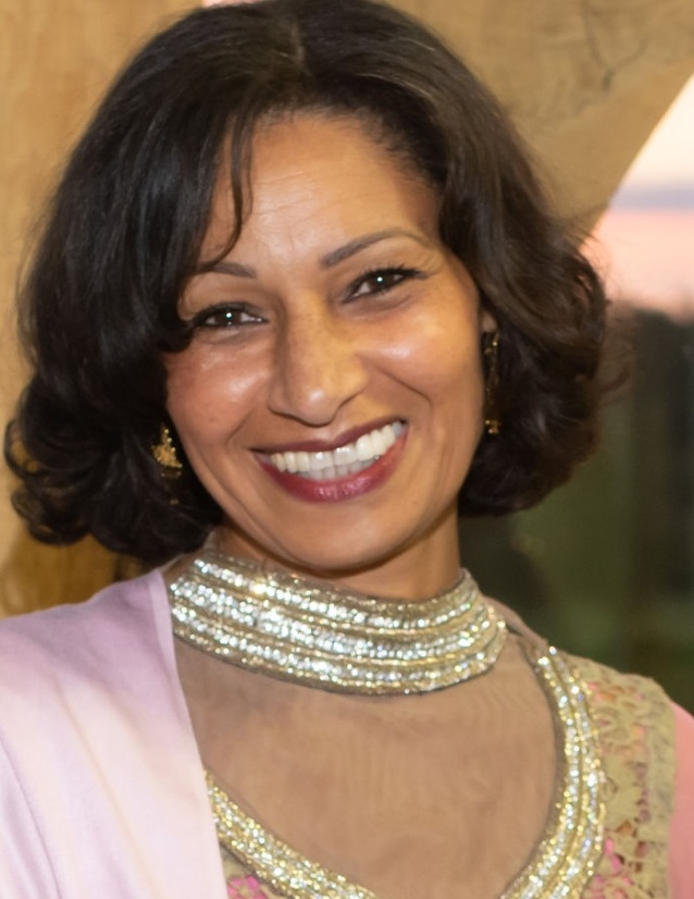 Woman with dark hair smiling at camera she is wearing a pink dress with silver and gold detailing 