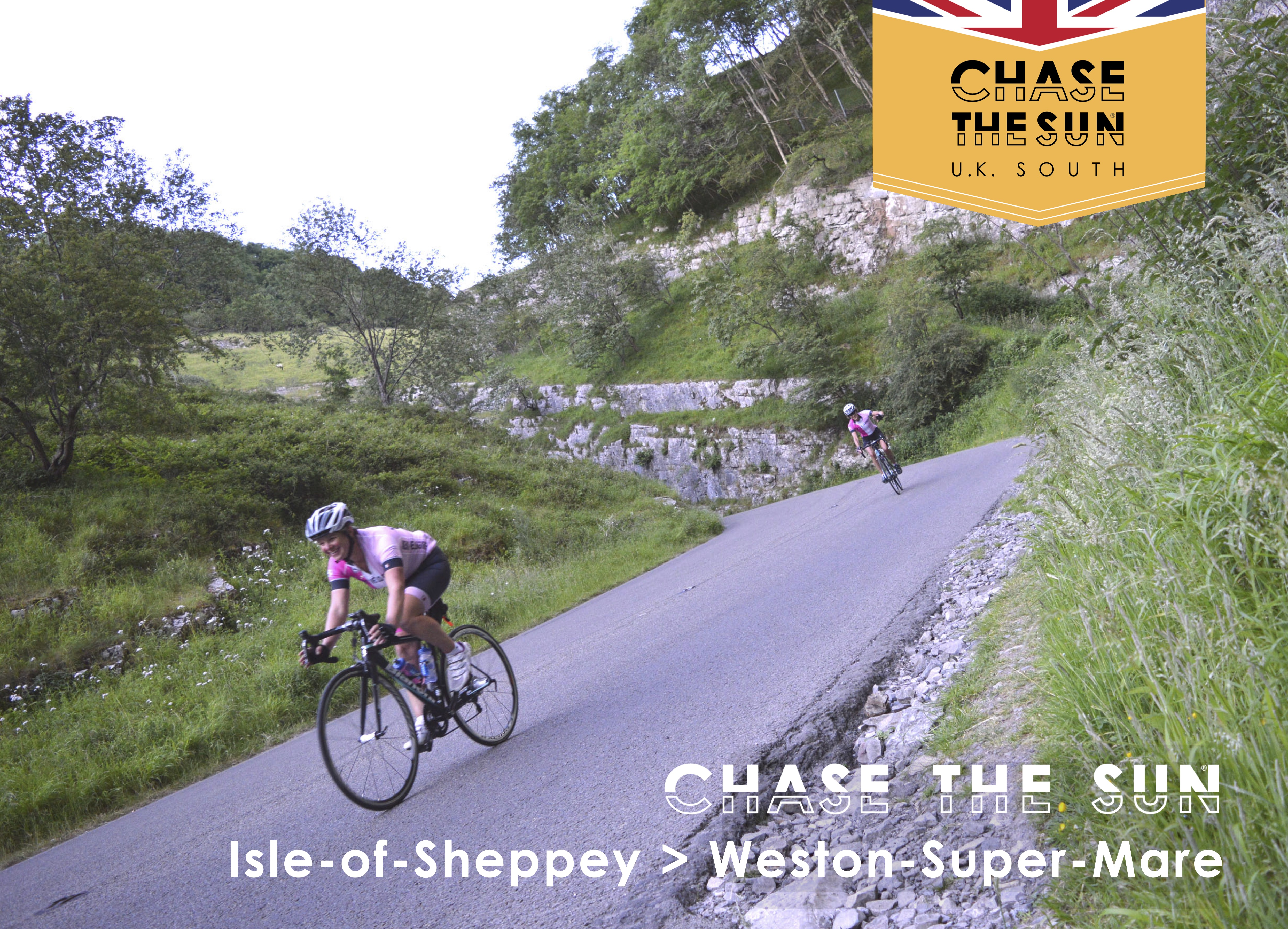 Two cyclists are riding downhill on a paved road through the countryside. They are wearing cycling gear like helmets and shorts. The image also features the Chase the Sun UK South logo and copy that says Chase the Sun Isle of Sheppey to Weston-Super-Mare.