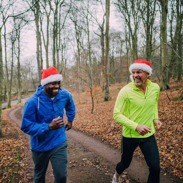 Two men running through the woods wearing Santa hats