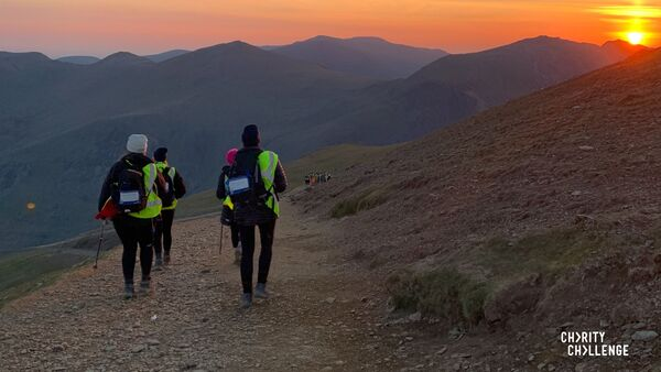 A group of people hiking down a rocky path as the sun is setting in the distance. 