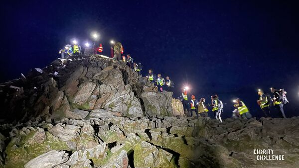 A group of hikers are climbing up a rocky pass at night. Many are wearing headlamps. 
