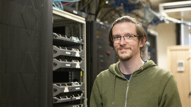 Phil, a Service Desk Analyst at Macmillan Cancer Support who works on a network server. He has short brown hair and is wearing a green jumper and glasses. 