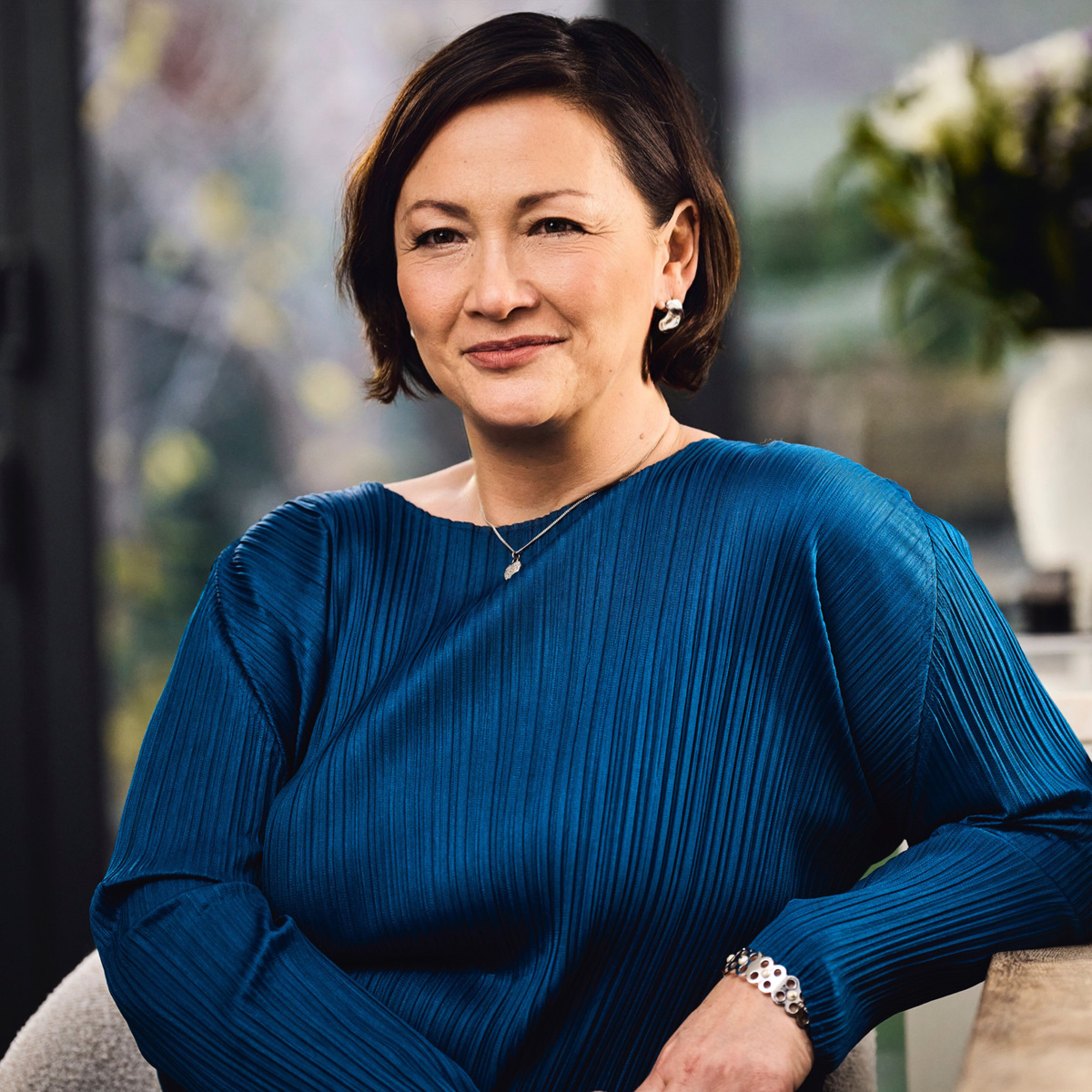 A woman wearing a silken blue top leans casually against a kitchen island