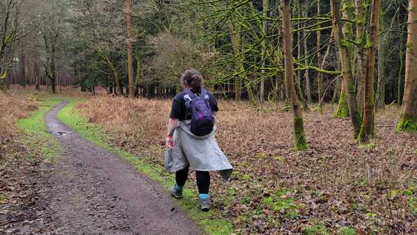 A person is hiking in Thetford Forest in Norfolk. They are following a muddy path and are wearing hiking shoes and attire.
