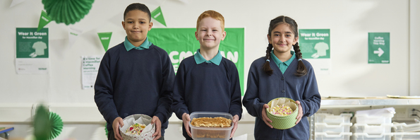 Three school children proudly holding the baked goods they've made for a school Coffee Morning