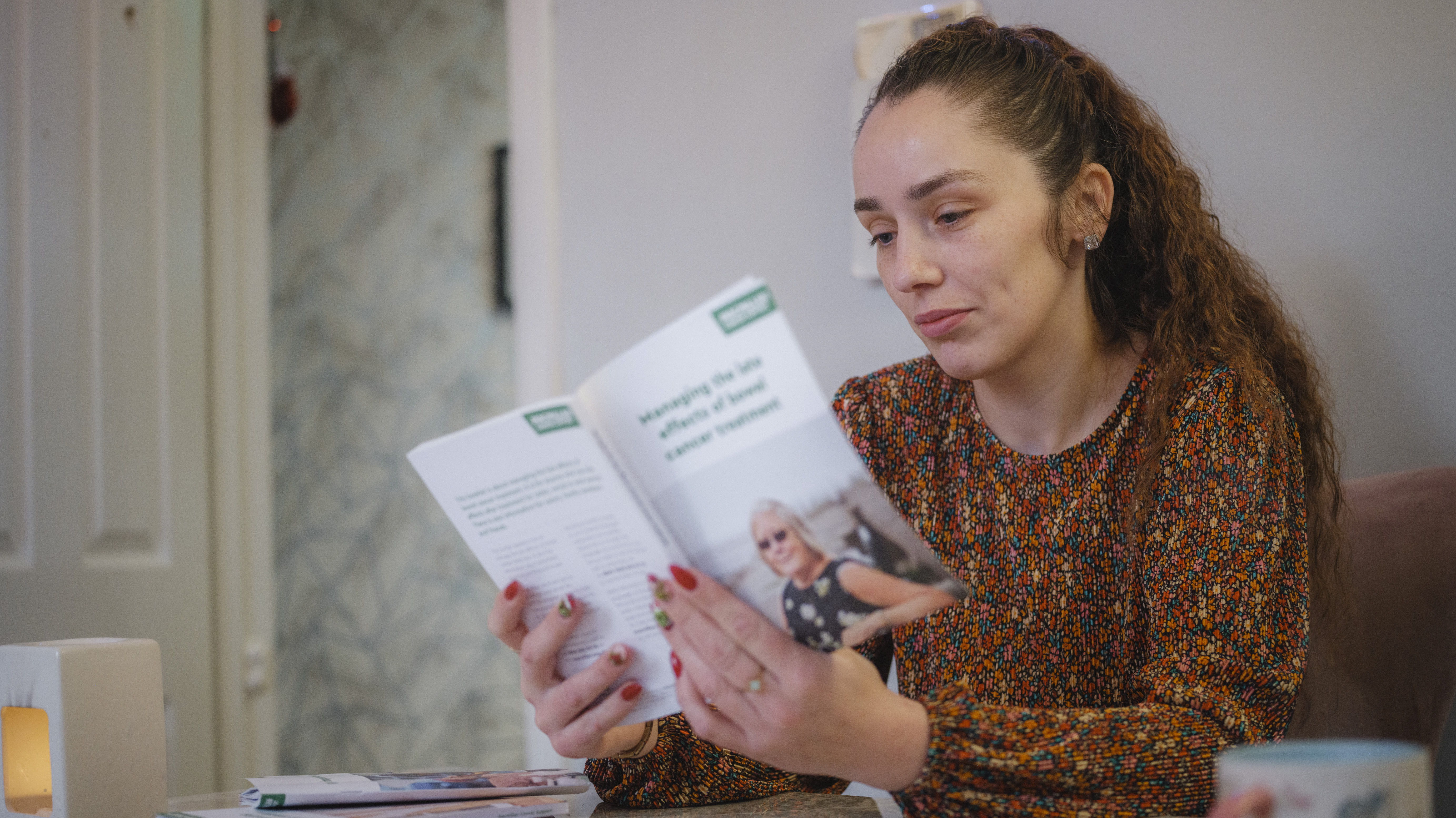 Jess is a lady with long brown hair, sat reading a Macmillan booklet.