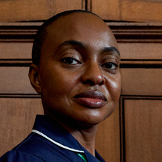 A nurse stands against a wood‑panelled wall,