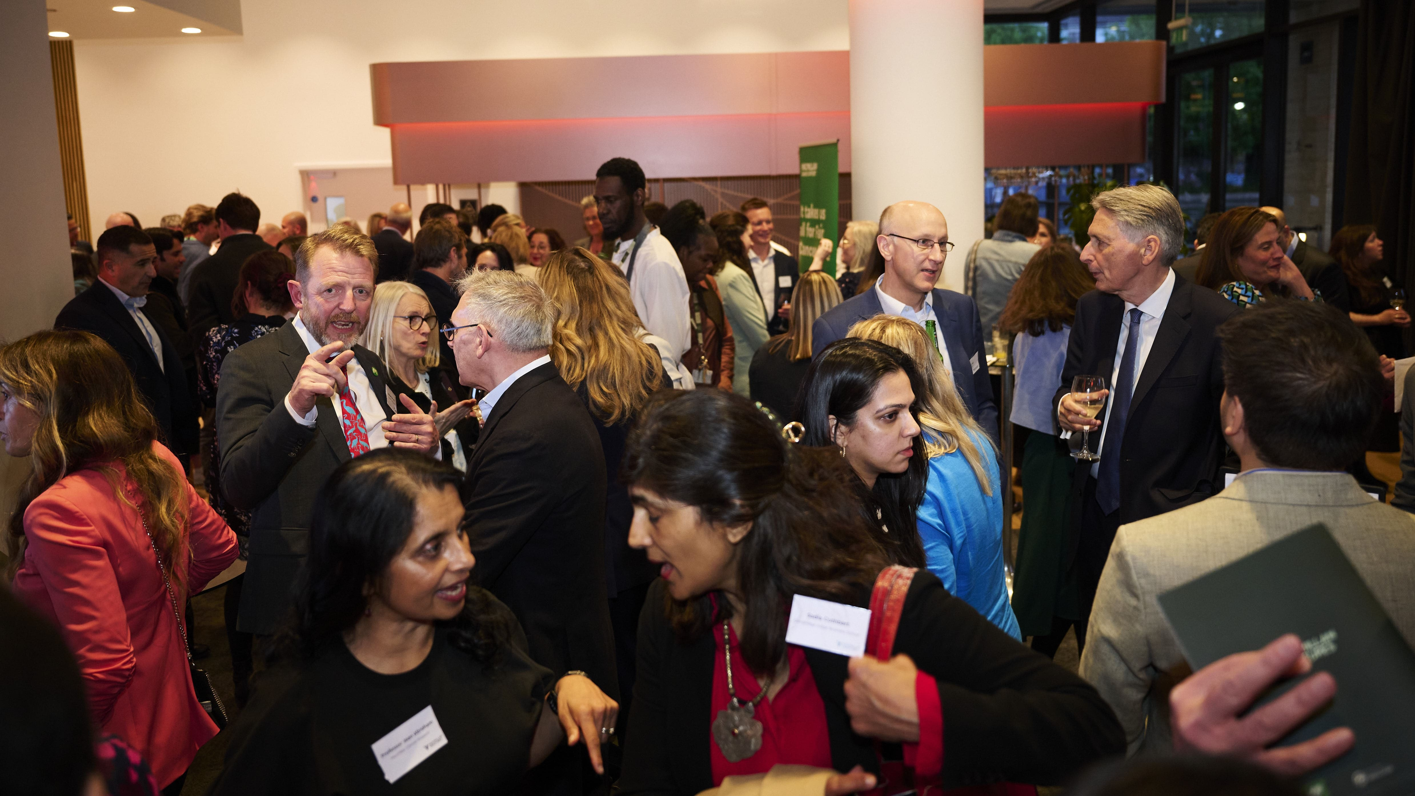 Crowded networking event with people in business attire talking in a modern indoor venue.