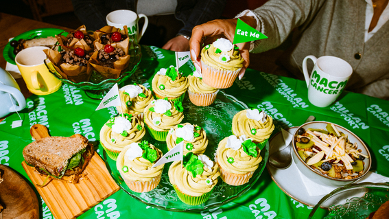 A bundle of yummy vanilla and matcha cupcakes are on top of a clear cake stand. The cupcakes are topped with tasty, rich frosting. 
