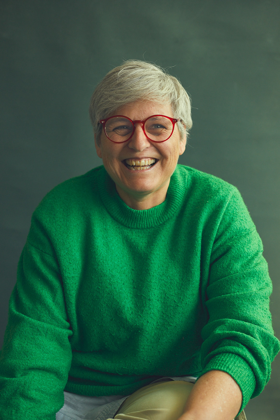 Zoe smiling while wearing a green jumper and red rimmed glasses