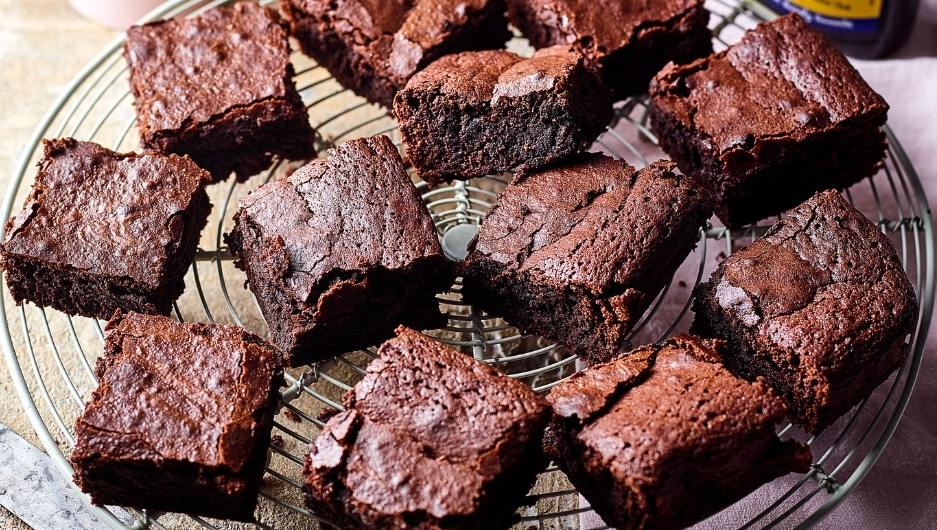 Fudgy chocolate brownies with crackled tops on a cooling rack, served with coffee, whipped cream, and Camp Coffee essence.