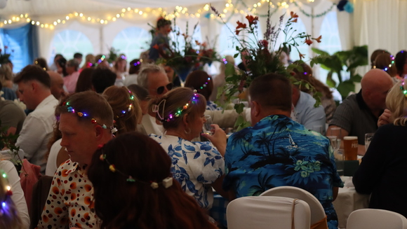 A large crowd of people at a fundraising event. They are sitting down at tables in a marquee.