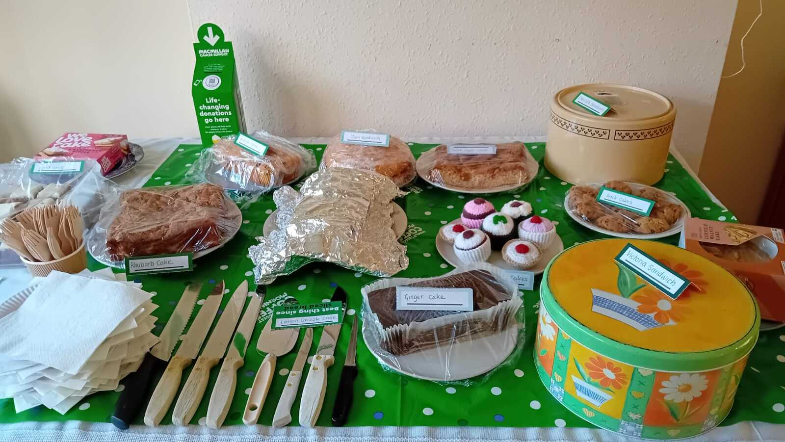 A table with different treats on display for a Coffee Morning. They different delicious options are labelled and there is cutlery on the table.