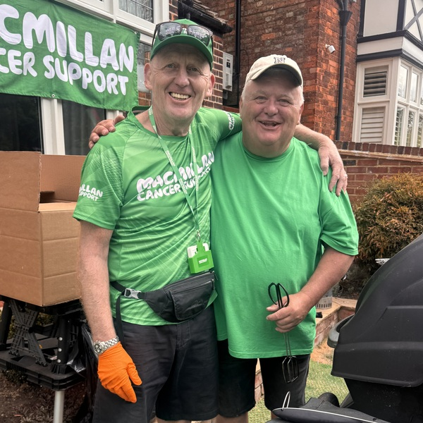 John, on left, pictured at the Bedford River Fest. He is standing with someone else and has one arm around them. He appears to be grilling a BBQ.