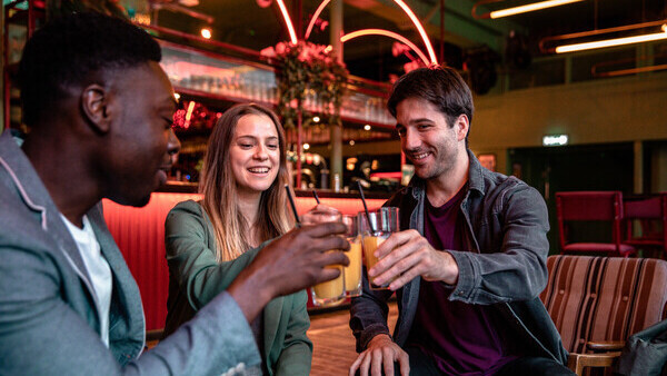  3 people in a bar clinking their glasses of orange juice together