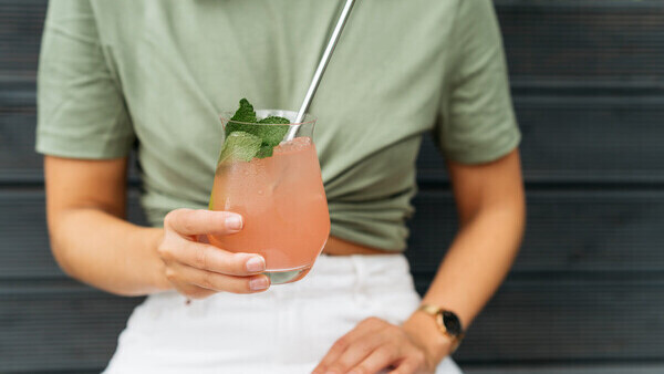 Someone holding up a pink mocktail with mint leaves and a metal straw.