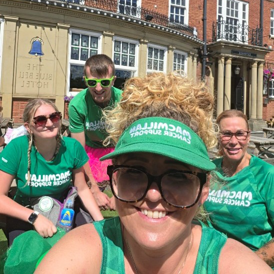 A selfie of a group of people outside a pub. They are dressed in all green in Macmillan gear.