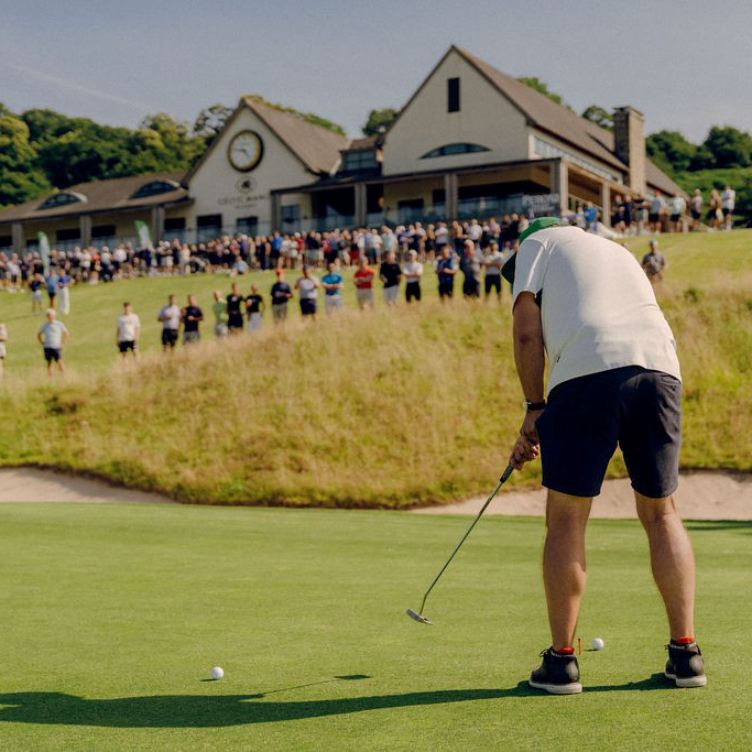 A person taking part in a golf charity day. The person is bent over hit the ball towards the hole.
