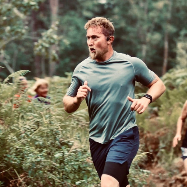 Gary is running on a trail in the woods. He is wearing fitness clothing.
