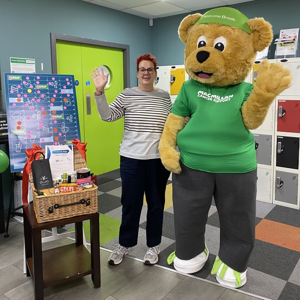 A person in a stuffed teddy bear costume is standing next to another person and they are waving. They are fundraising for Macmillan.