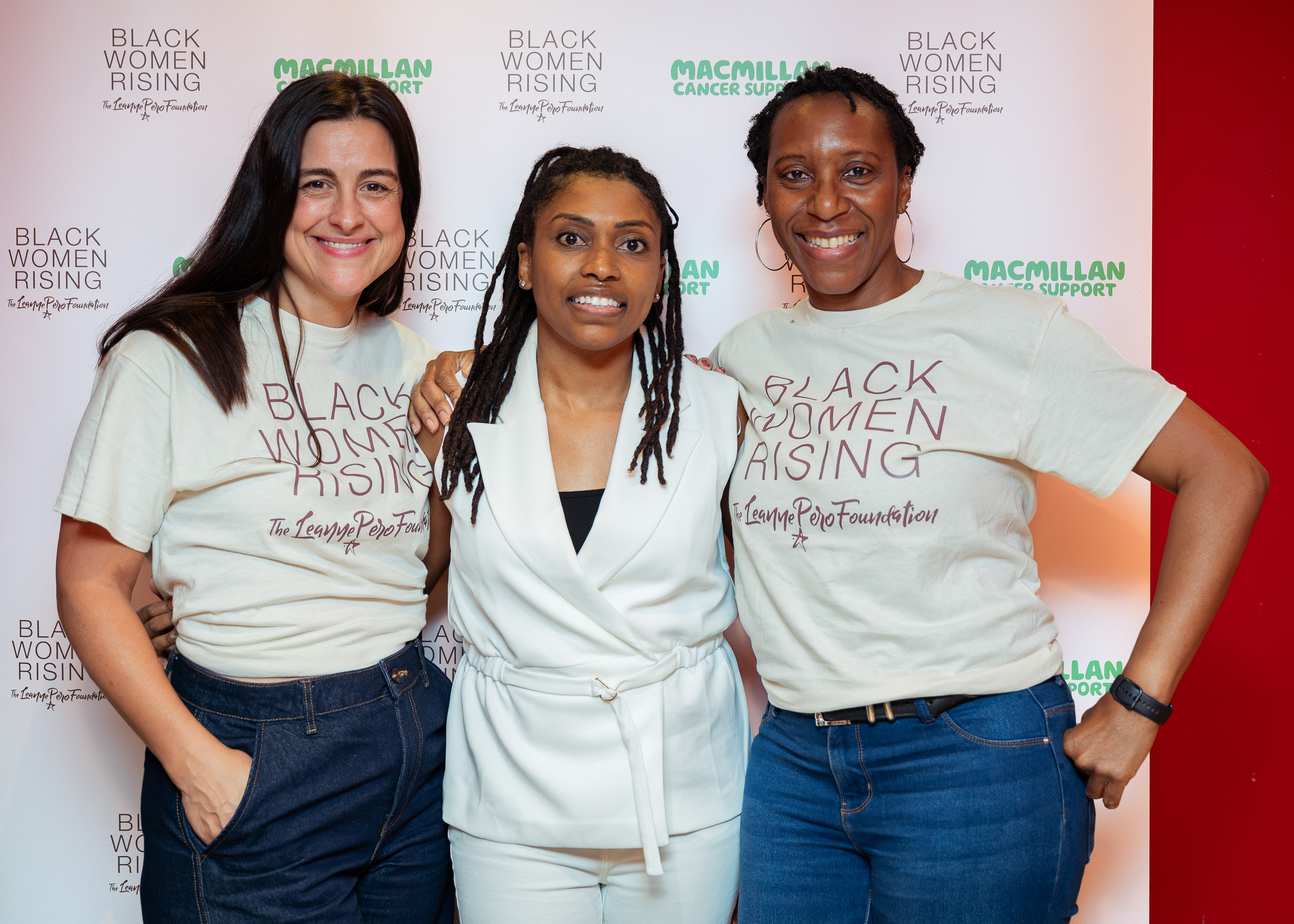 Three women pose together in front of a Black Women Rising and Macmillan Cancer Support event backdrop.