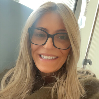 A person wearing glasses sitting in a treatment chair near an IV drip during cancer treatment.